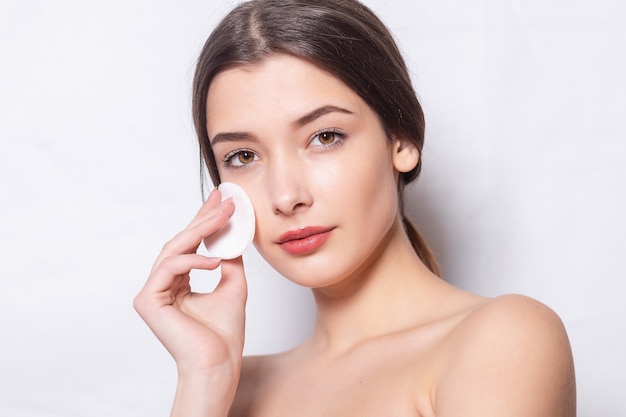 Mujer joven cuida la piel de la cara. Chica quita el maquillaje con una bola de algodón de la cara. Mujer joven limpia la piel del cosmético con un hisopo de algodón. Concepto de cuidado de la piel.