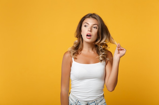 Mujer joven curiosa con ropa informal ligera posando aislada en un fondo naranja amarillo en el estudio. Gente emociones sinceras concepto de estilo de vida. Simulacros de espacio de copia. Manteniendo la boca abierta, mirando a un lado.