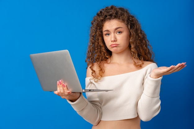 Mujer joven curlyhaired sosteniendo el portátil contra el fondo azul.