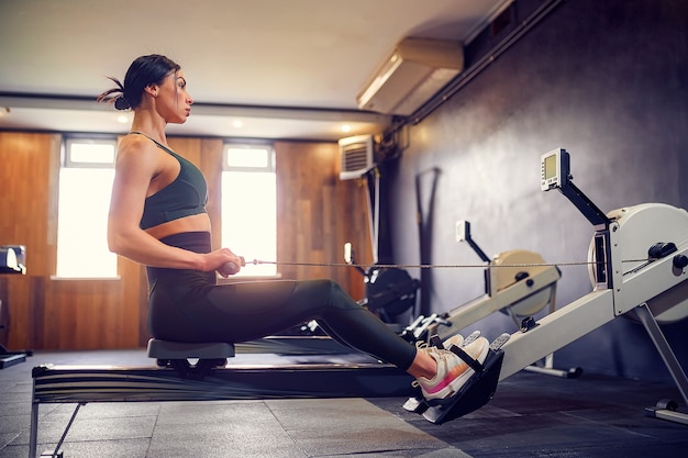 Mujer joven decidida que trabaja en la máquina de la fila en el gimnasio