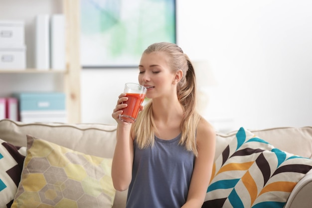 Mujer joven degustación de jugo fresco sentado en el sofá en la sala de estar