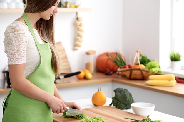 Mujer joven en el delantal verde cocinando en la cocina. Ama de casa mezclando ensalada fresca.