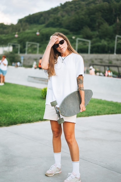 Mujer joven delgada con cabello largo y rubio con longboard en el skatepark al aire libre al atardecer