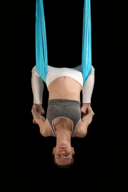 Mujer joven demuestra asanas invertidas durante fly yoga Chica practica yoga antigravedad al revés Fondo negro