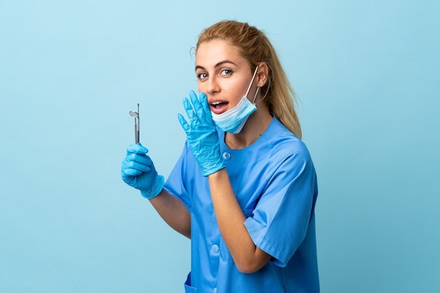 Mujer joven dentista sosteniendo herramientas aisladas susurrando algo