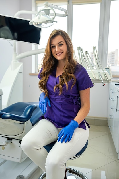 Mujer joven dentista en uniforme y guantes de protección posando sola en la atención médica de la clínica