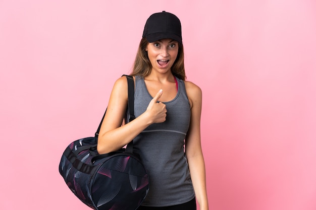 Mujer joven deporte con bolsa de deporte aislada en rosa con expresión facial sorpresa