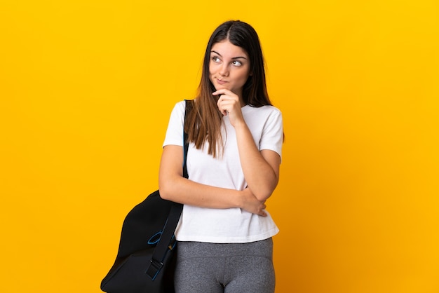 Mujer joven deporte con bolsa de deporte aislado en amarillo con dudas y pensamiento