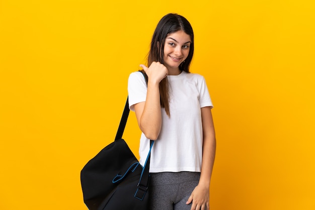 Mujer joven deporte con bolsa de deporte aislado en la pared amarilla apuntando hacia el lado para presentar un producto