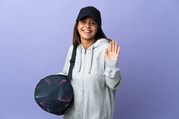 Mujer joven deporte con bolsa de deporte saludando con la mano con expresión feliz