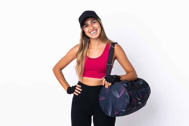 Mujer joven deporte con bolsa de deporte sobre blanco aislado posando con los brazos en la cadera y sonriendo