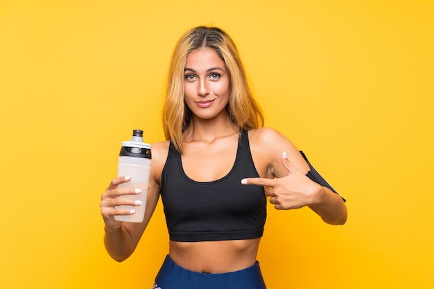 Mujer joven del deporte con una botella de agua sobre la pared aislada