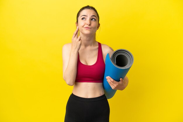 Mujer joven deporte que va a clases de yoga mientras sostiene una estera con los dedos cruzando y deseando lo mejor