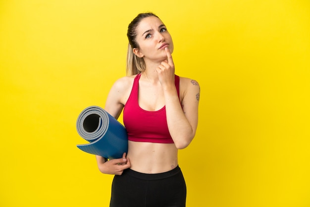 Foto mujer joven deporte que va a clases de yoga mientras sostiene una estera que tiene dudas mientras mira hacia arriba