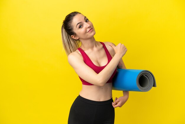 Mujer joven deporte que va a clases de yoga mientras sostiene una estera