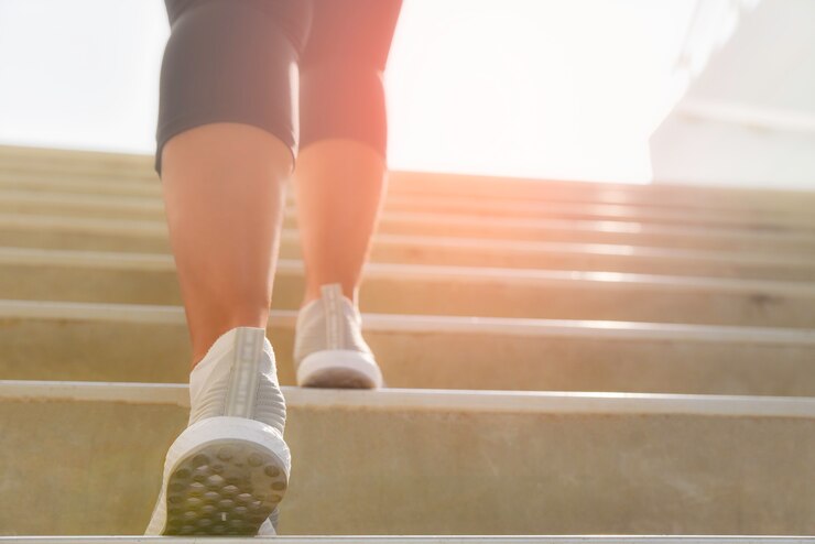 Mujer joven del deporte que corre para arriba en las escaleras de piedra con el fondo del punto del sol. Concepto de entrenamiento y dieta.