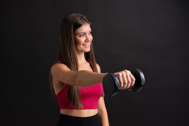 Mujer joven del deporte que hace levantamiento de pesas sobre la pared negra aislada