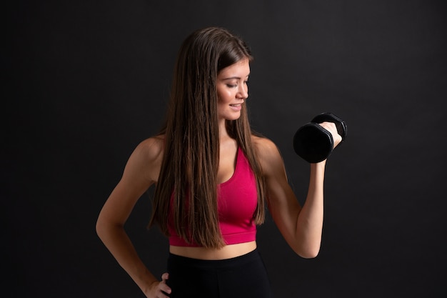 Mujer joven del deporte que hace levantamiento de pesas sobre la pared negra aislada