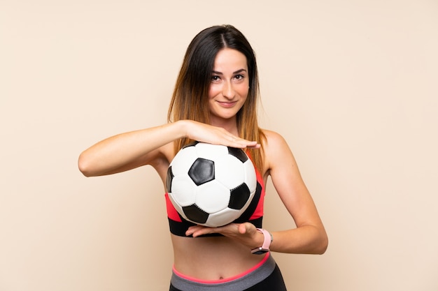 Mujer joven del deporte sobre la pared aislada que sostiene un balón de fútbol