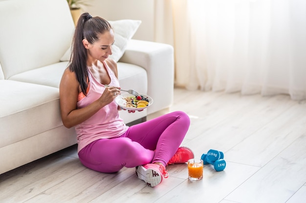 Mujer joven deportiva comiendo avena con bayas y frutas después de un entrenamiento