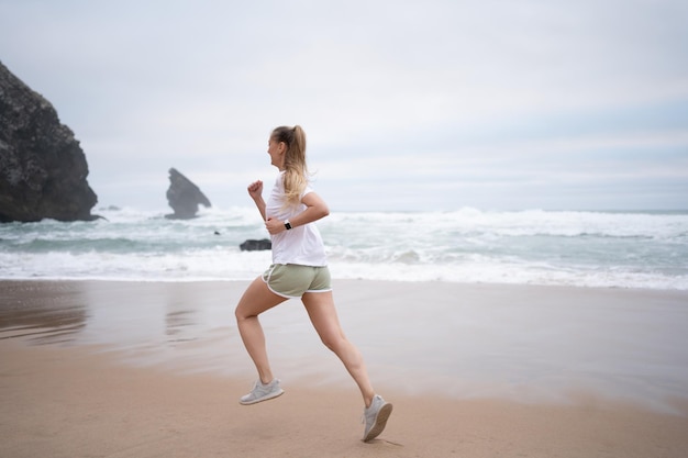 Mujer joven deportiva corriendo en la playa de arena a lo largo del mar.