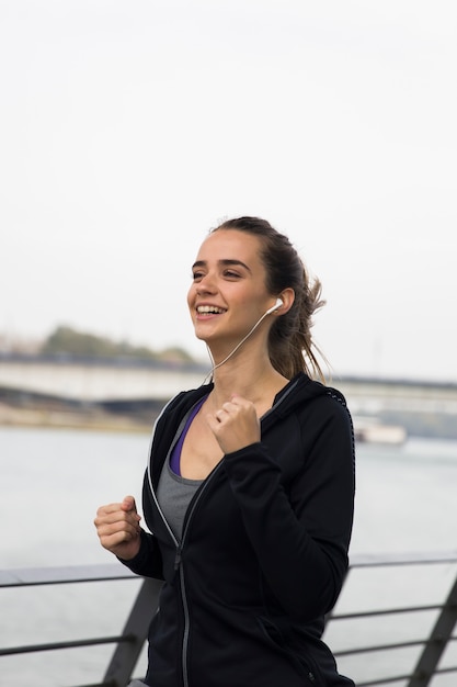 Mujer joven deportiva corriendo por el río y escuchando música con auriculares