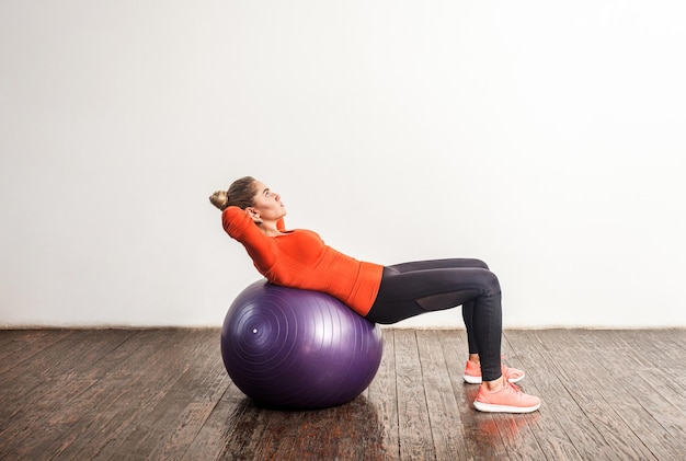 Mujer joven deportiva delgada acostada en una gran pelota de goma de fitness estirando y ejercitando los músculos del abdomen