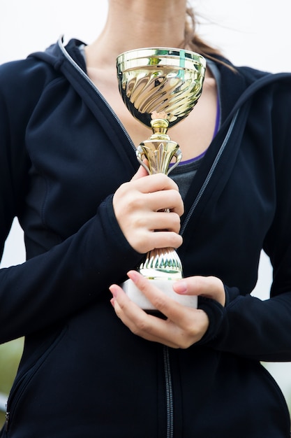 Mujer joven deportiva feliz que sostiene el trofeo de oro