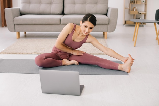 Mujer joven deportiva practicando yoga frente a la computadora portátil viendo tutoriales en línea