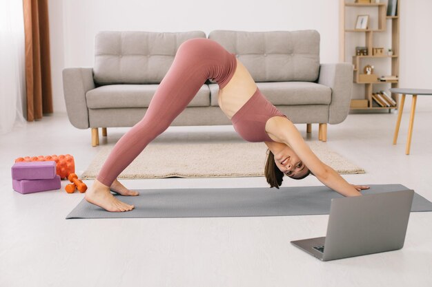 Mujer joven deportiva practicando yoga frente a la computadora portátil viendo tutoriales en línea