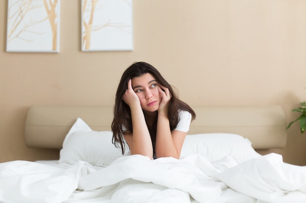 Foto mujer joven en depresión sentada en la cama en casa