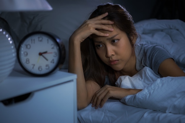 Mujer joven deprimida acostada en la cama no puede dormir por insomnio