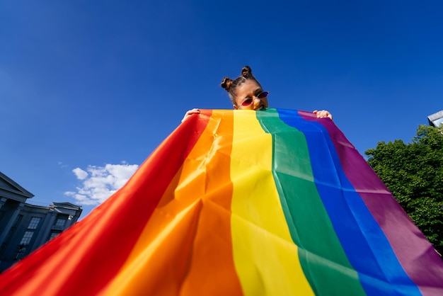 Una mujer joven desarrolla una bandera del arco iris contra el cielo