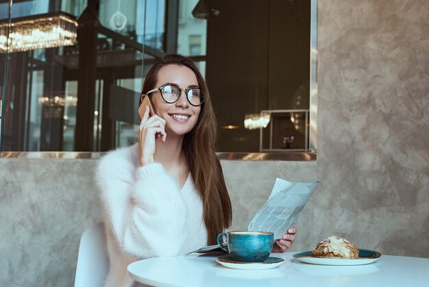 Mujer joven desayunando con café y croissant leyendo