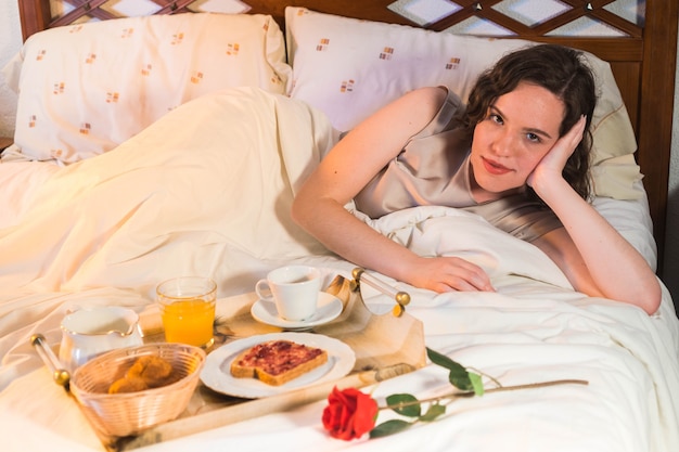 Mujer joven con un desayuno romántico con cupcakes de tostadas de café de jugo de naranja y una rosa