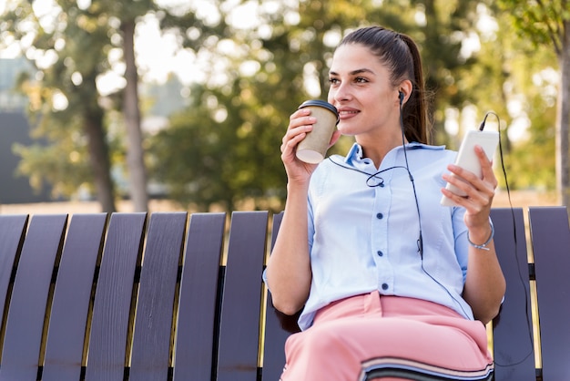 Foto la mujer joven descansa en el parque del otoño en el banco después de un paseo y escucha la música en el teléfono.