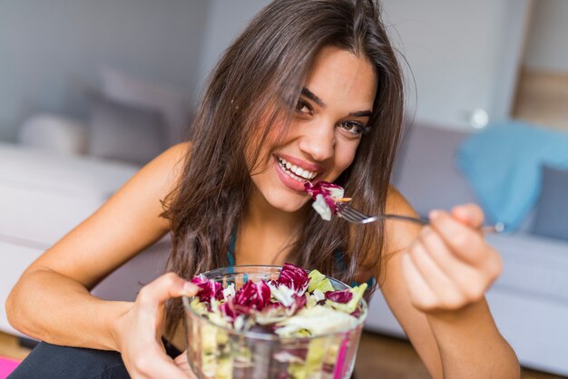 Foto una mujer joven está descansando y comiendo una ensalada saludable después de un entrenamiento y parpadeando sus ojos.