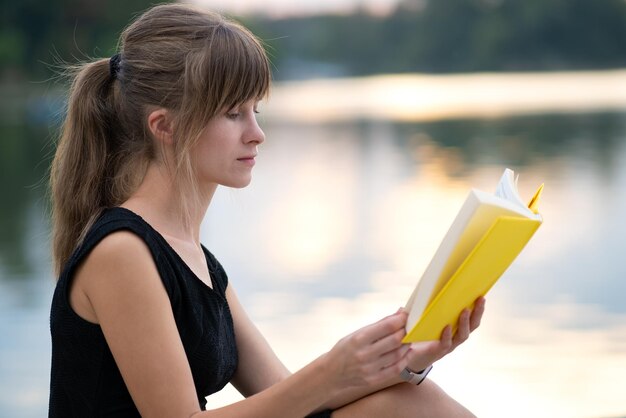 Mujer joven descansando en el parque de verano leyendo un libro. Concepto de educación y sudy.