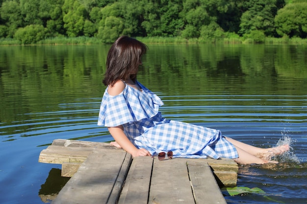 Mujer joven descansando sobre un puente de madera y moja los pies en el río Sunny sumer day