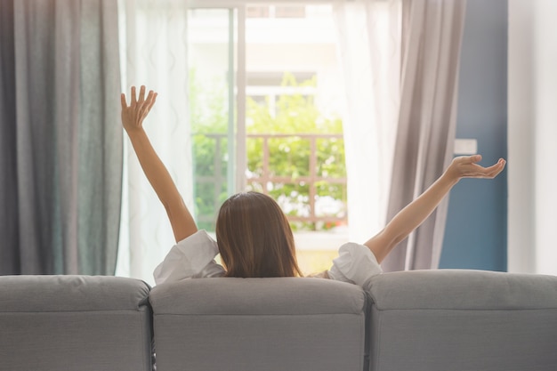 Mujer joven descansando en el sofá en casa acogedora y mirando afuera en la sala de estar