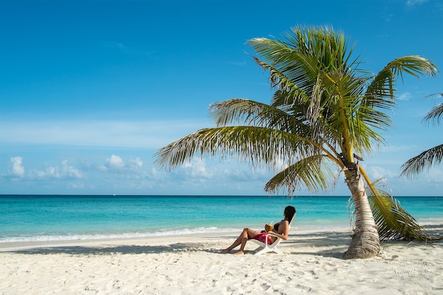 Mujer joven descansando en una tumbona bajo una palmera junto al mar