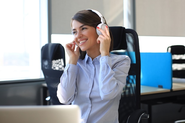 Mujer joven con un descanso y escuchando música en auriculares sentado en el lugar de trabajo.