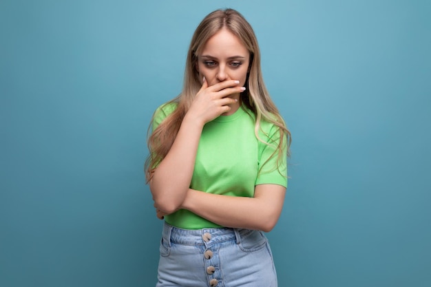 Mujer joven desconcertada en atuendo casual razonando cubriendo su boca con su mano en un azul aislado