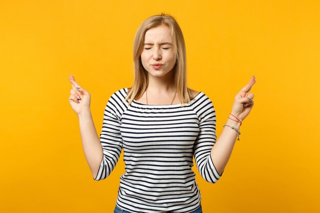 Mujer joven desconcertada mordiéndose los labios, esperando un momento especial, manteniendo los dedos cruzados, pidiendo deseos aislados en un fondo naranja amarillo. Emociones sinceras de la gente, concepto de estilo de vida. Simulacros de espacio de copia.