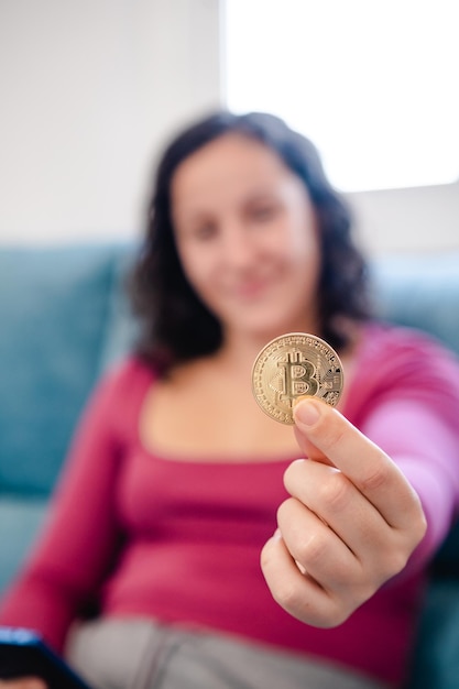 Mujer joven desenfocada y no reconocida con una moneda de bitcoin en la mano en casa