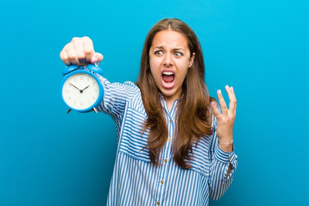 Mujer joven con despertador pared azul