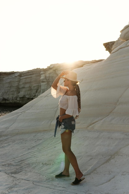 Foto mujer joven despreocupada con sombrero de paja posando en piedras blancas en la orilla rocosa