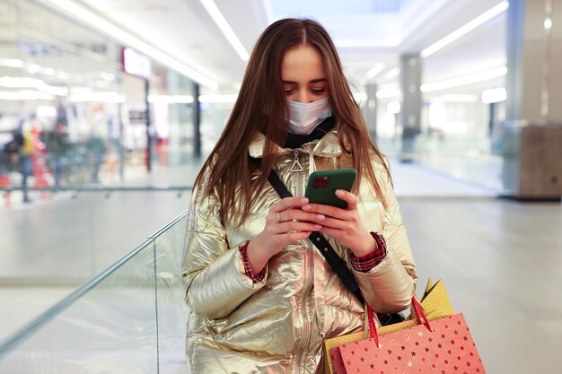 Mujer joven después de ir de compras escribiendo en su teléfono en un centro comercial