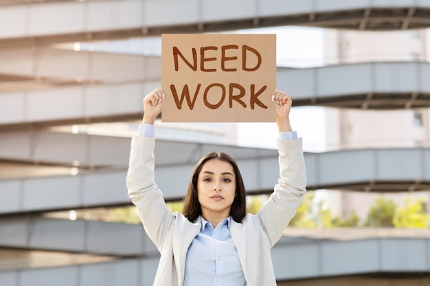 Foto una mujer joven determinada en vestimenta de negocios sosteniendo un cartel que dice que necesita trabajo