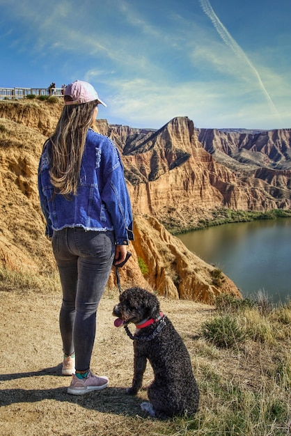 Mujer joven por detrás y con perro mirando un paisaje escénico de cañones.